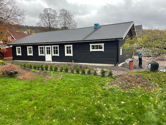 Färdigt mörkt trähus med vita fönster och tegeltak.