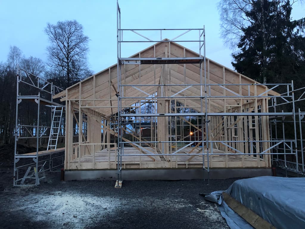 Trästomme till ett hus under byggnation, med byggställning runt huset.